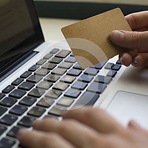 Credit card in hand and entering security code using laptop keyboard.