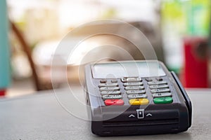 Credit card machine with car refueling petrol at gasoline station in background.