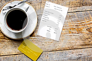 Credit card for paying, coffee and check on cafe wooden desk background top view mock up