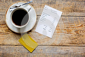 Credit card for paying, coffee and check on cafe wooden desk background top view mock up