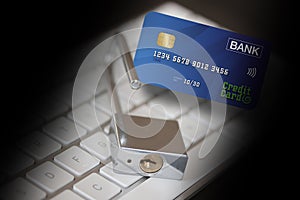 Credit card, stainless padlock and a credit card in front of a computer keyboard surrounded with a black shadow. Credit card data