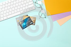 Credit cards, computer keyboard and glasses on blue background, flat lay. Space for text