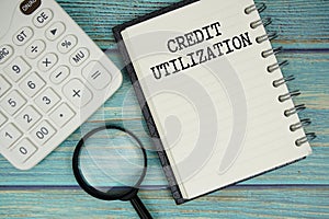 Credit Utilization text on notepad with magnifying glass and calculator on wooden background
