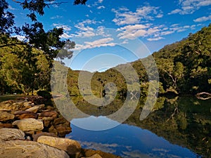 Beautiful view of creek with reflections blue sky, light clouds, fog, mountains and trees on water