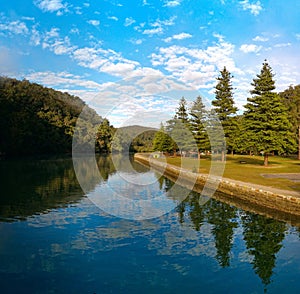 Beautiful view of creek with reflections blue sky, light clouds, fog, mountains and trees on water