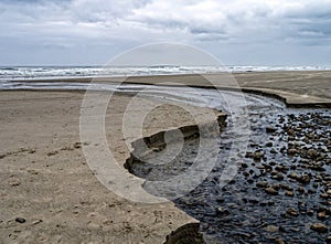 A creek flows into the Pacific Ocean on an overcast day near Yachats, Oregon, USA