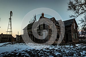 Creepy abandoned house with windmill in rural setting in winter with snow