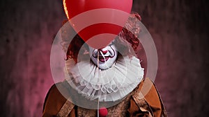 Creepy clown releases a red ball and shows his face. Clown in a colorful makeup