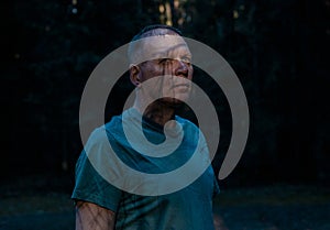 Creepy man portrait with shadow on face in dark forest. Scary look of mature senior man. Madness, horror and halloween