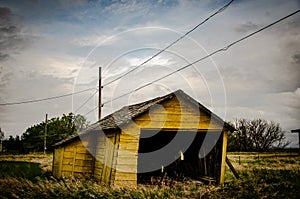 Creepy, old and aged abandoned wooden barn in a field under the cloudy and rainy sky