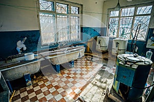 Creepy old laundry room with a dirty floor and broken wash machines and bathes in an abandoned psychiatric hospital.