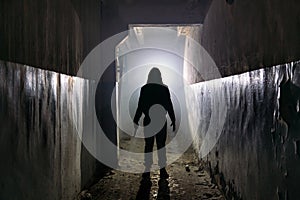 Creepy silhouette of unknown man with knife in dark abandoned building. Horror about maniac concept