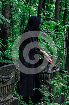 Creepy witch in black in spooky abandoned cemetery