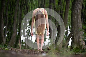 Creepy woman with long hair standing bent down in moody dark forest