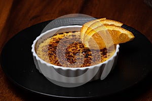 Creme brulee, burnt cream with orange on the dark wood table.