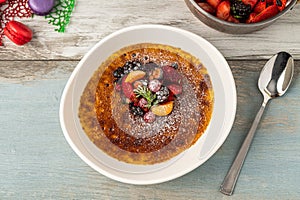 Creme brulee decorated with fruits and powdered sugar on a wooden table
