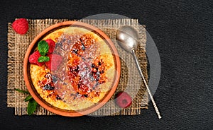 Creme brulee dessert of cream and cane sugar with fresh raspberries and mint leaves on a dark table, layout with copy space.