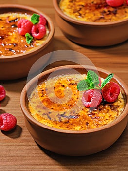 Creme brulee desserts with cream and cane sugar with fresh raspberries and mint leaves in clay bowls on a dark vintage table,