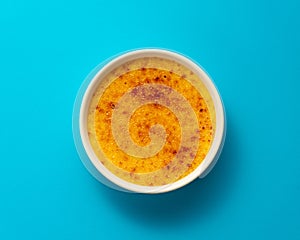 Creme brulee in ramekin isolated on bright blue color background. Top view photo