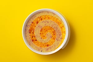 Creme brulee in ramekin isolated on bright yellow color background. Close up photo