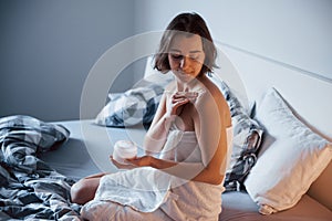 Creme on the shoulders. Time for a make up. Woman sits on the bed and use cosmetics to clean her skin