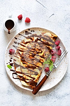 Crepe with chocolate paste, banana and raspberries on a concrete background. Tasty breakfast photo