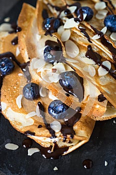 Crepes with blueberries almond flakes and chocolate sauce on black.