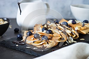 Crepes with blueberries almond flakes and chocolate sauce on black.