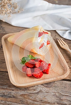 Crepes cake roll cream cheese with strawberry on wood plate.