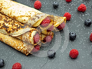 Crepes filled with jam and fresh raspberry and blueberries on slate