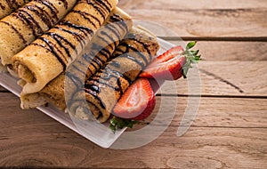 Crepes with nutella and strawberries. Rustic wooden background.