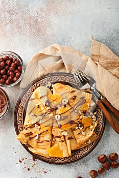 Crepes suzette with oranges and chocolate. Thin crepes with chocolate spread, hazelnuts and orange slices fruit in plate for