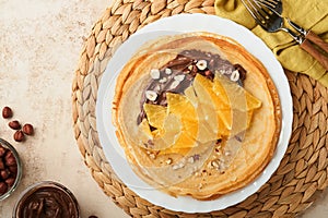 Crepes suzette with oranges. Thin crepes with chocolate spread, hazelnuts and orange slices fruit in white plate for breakfast on