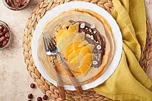 Crepes suzette with oranges. Thin crepes with chocolate spread, hazelnuts and orange slices fruit in white plate for breakfast on