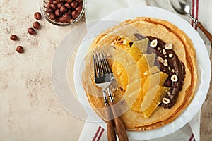Crepes suzette with oranges. Thin crepes with chocolate spread, hazelnuts and orange slices fruit in white plate for breakfast on
