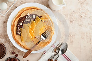 Crepes suzette with oranges. Thin crepes with chocolate spread, hazelnuts and orange slices fruit in white plate for breakfast on