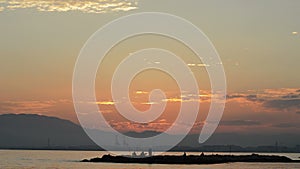 Crepuscule sunset with fishers in the rocks and port cranes at background