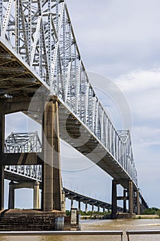 The Crescent City Connection bridge over the Mississippi River with lush green trees, plant and grass, blue sky and clouds