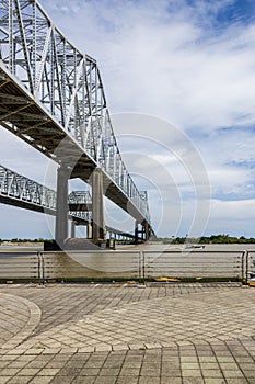 The Crescent City Connection bridge over the Mississippi River with lush green trees, plant and grass, a boat sailing on the water