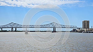The Crescent City Connection bridge over the Mississippi River with lush green trees, plant and grass boats sailing, blue sky