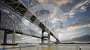 The Crescent City Connection bridge over the Mississippi River with lush green trees and plants and powerful clouds at sunset