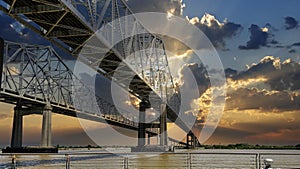 The Crescent City Connection bridge over the Mississippi River with lush green trees and plants and powerful clouds at sunset