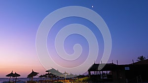 Crescent moon on beautiful night sky over beach with straw umbrellas