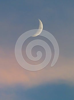 Crescent moon in a blue sky with pale pink clouds