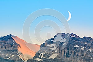 Crescent moon over snow capped mountains - Lake Louise - Canada photo