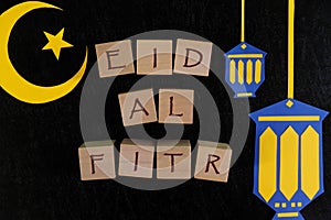 Crescent moon, star and lantern decoration with text on wooden blocks flat lay in dark black background. Eid al fitr celebration