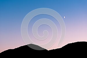 Crescent moon in sunset sky above sillhouette of mountains