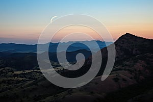 crescent moon between two hill peaks