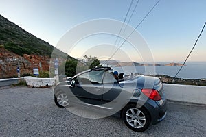 Crete. Greece - April 1, 2019: The girl and the cabriolet stand in front of a stunning panoramic view. Sea and winding mountain