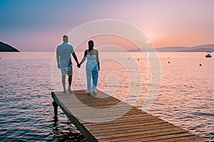 Crete Greece, young romantic couple in love is sitting and hugging on wooden pier at the beach in sunrise time with